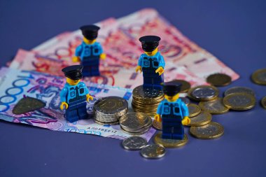 Almaty, Kazakistan - 11.26.2025: Banknotların arka planında 10 sentlik madeni parası olan bir güvenlik görevlisi veya polisin sembolik figürü. Ceza, ceza, ödül..