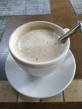 Yüzeyde köpüklü bir fincan kahve. Masanın üstünde yakın plan bir fincan çay tabağı.