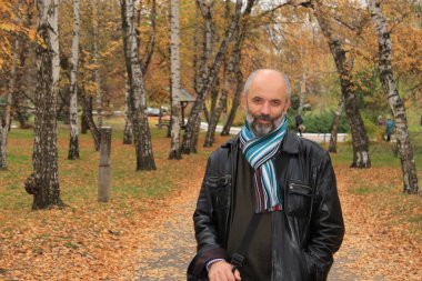 Güz parkında boynundaki atkıyla sakallı, olgun bir adam.