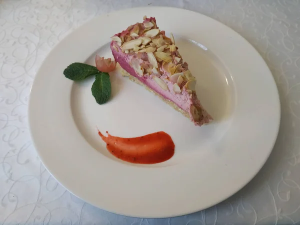 Slice of fruit-mousse cake. Served with a mint leaf, berry jam