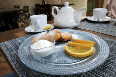 Pudra şekerli peynirli kekler. Bir kase ekşi krema ve üç dilim portakalla servis edilir.