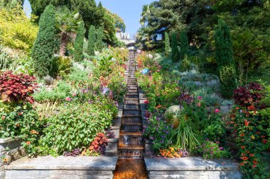 Teraslı çiçek bahçeleri ve Mainau Adası 'ndaki yuvarlak bir havuza taştan bir şelale şelalesi, güneşli bir günde bereketli Akdeniz tarzı bitki örtüsü sergiliyor. Konstanz, Almanya