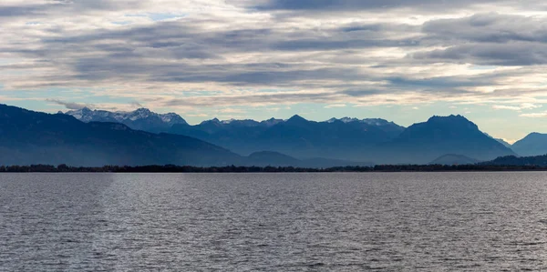 Almanya 'nın Lindau kenti yakınlarındaki Constance Gölü' nün (Bodensee) karanlık suları üzerindeki dramatik panoramik manzara, İsviçre veya Avusturya Alpleri 'nin silueti bulutlu ve kasvetli bir gökyüzü altında