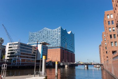 HAMBURG, GERMANY - 12 Ağustos 2024: Hamburg 'un HafenCity kentindeki Elbphilharmonie konser salonu ve modern konut binaları, küçük bir iskeleden ve su yansımalarıyla deniz kıyısından izlendi