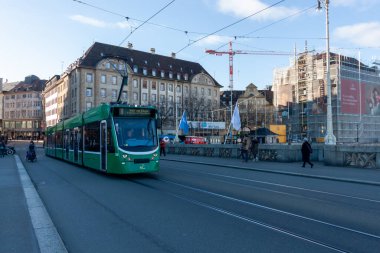 BASEL, SWitzERLAND - 16 Aralık 2024: Modern yeşil bir tramvay (Hat 8) İsviçre 'nin Basel kentindeki bir köprüden geçerek tarihi binaları ve iskeleli aktif bir inşaat alanını geçer.