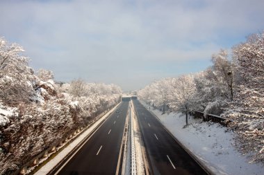 Geniş, çok şeritli otoyol, bulutlu bir gökyüzünün altında yoğun karla kaplı ağaçlarla dolu bir orman arazisinden geçen kardan temizlendi.