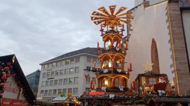 BASEL, SWitzERLAND - 10 Aralık 2025: ışıklarla süslenmiş uzun, geleneksel bir Alman ahşap Noel piramidi, Basel Noel Pazarı 'nda müze binasının yanında duruyor.