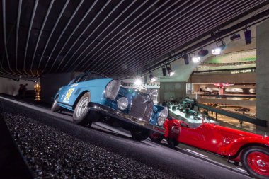 STUTTGART, GERMANY - 18 Ekim 2025: Mavi Mercedes-Benz 300 SE rali arabası ve Stuttgart Mercedes-Benz Müzesi 'ndeki bankalı pistte kırmızı vintage yarış aracı. İkonik motor sporu mirası ve klasik mühendislik Almanya 'da sergileniyor