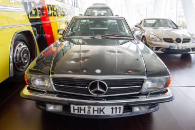 STUTTGART, GERMANY - 18 Ekim 2025: Mercedes-Benz Müzesi 'nde (R107) sarı takım otobüsü ve arka planda diğer roadster' larla klasik siyah bir Mercedes-Benz SL 'nin ön görüntüsü
