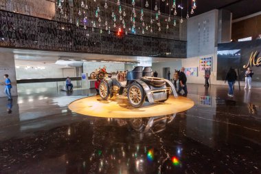 STUTTGART, GERMANY - 18 Ekim 2025: Stuttgart 'taki Mercedes-Benz Müzesi' nde parlayan dairesel bir projektörde antik motorlu araç. Yansıtıcı zeminli modern galeri ve arka planda ziyaretçiler