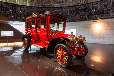 STUTTGART, GERMANY - OCTOBER 18, 2025: Red antique motorized bus with wooden wheels and brass lamps, exhibited in the Mercedes-Benz Museum in Stuttgart, showcasing early 20th-century public transportation history