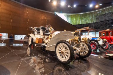 STUTTGART, GERMANY - 18 Ekim 2025: Stuttgart 'taki Mercedes-Benz Müzesi' nin yansıtıcı zemininde sergilenen büyük farları ve ahşap tekerlekleri olan pirinç çağından kalma zarif beyaz antika bir araba