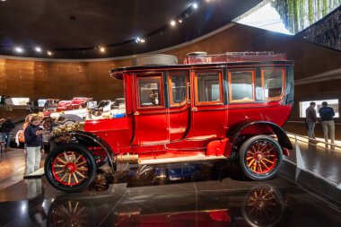 STUTTGART, GERMANY - OCTOBER 18, 2025: Red antique motorized bus with wooden wheels and brass lamps, exhibited in the Mercedes-Benz Museum in Stuttgart, showcasing early 20th-century public transportation history
