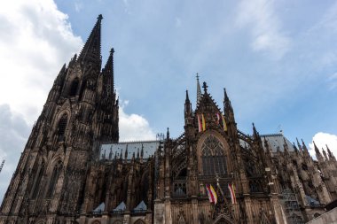 COLOGNE, ALMANY - 31 Mayıs 2024: Almanya 'da Gotik cepheyi ve Köln Katedrali' nin (Kolner Dom) ikiz kuleleri. Bulutlu mavi gökyüzünün altında bayraklarla UNESCO Dünya Mirası sahasının görkemli manzarası