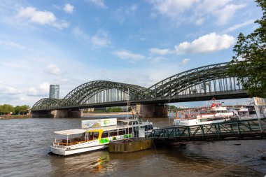 COLOGNE, GERMANY - 31 Mayıs 2024: Ren Nehri 'ne tarihi Hohenzollern Köprüsü' nün arka planında Almanya 'nın Köln kentindeki turistik gezi tekneleri yanaştı
