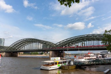 COLOGNE, GERMANY - 31 Mayıs 2024: Ren Nehri 'ne tarihi Hohenzollern Köprüsü' nün arka planında Almanya 'nın Köln kentindeki turistik gezi tekneleri yanaştı