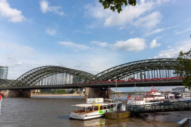COLOGNE, GERMANY - 31 Mayıs 2024: Ren Nehri 'ne tarihi Hohenzollern Köprüsü' nün arka planında Almanya 'nın Köln kentindeki turistik gezi tekneleri yanaştı