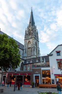 AACHEN, ALMANY - 31 Mayıs 2024: Aachen, Almanya 'nın merkezindeki yüksek Gotik kuleleri ile St. Foillan Kilisesi. Katedrale bitişik tarihi dini mimari, sokak seviyesinde dükkanlar ve akşam atmosferiyle