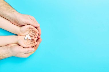 Adult and child hands holding white dove bird on blue background, international day of peace or world peace day concept.