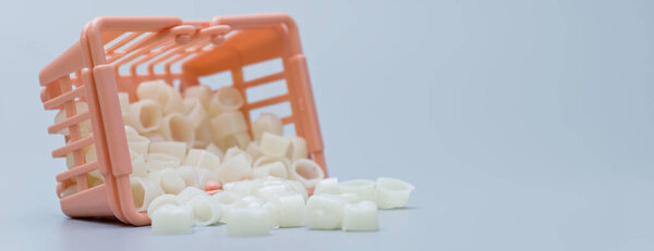 Пластиковые зубные коронки вываливаются из опрокинутой миниатюрной корзины, символизируя стоматологическую помощь, варианты лечения и расходы на здравоохранение.