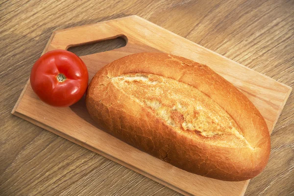 Pan fresco y tomate sobre una mesa de madera . — Foto de Stock