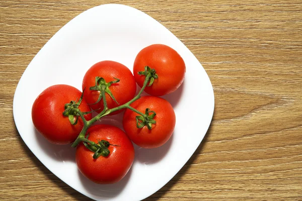 Tomates rojos frescos en plato blanco sobre mesa de madera — Foto de Stock