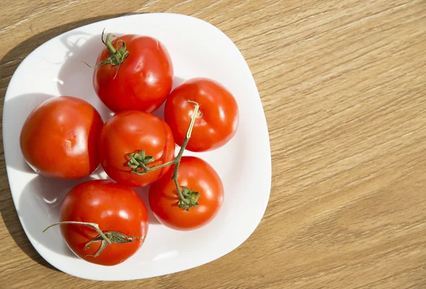 Tomates rojos frescos en plato blanco sobre mesa de madera — Foto de Stock