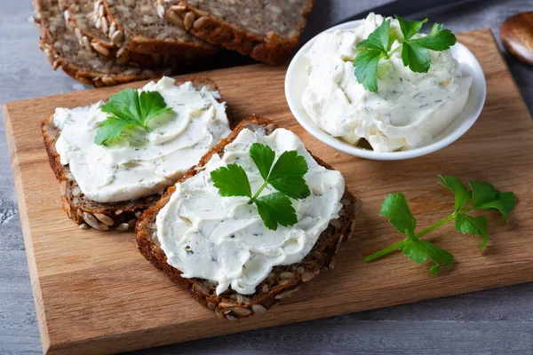 Ev yapımı ekmek, kaymak peyniri, ricotta ve bitkilerle ahşap bir kesim tahtasından. Yeşil otlarla süslenmiş.