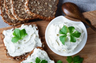 Ev yapımı ekmek, kaymak peyniri, ricotta ve bitkilerle ahşap bir kesim tahtasından. Yeşil otlarla süslenmiş.
