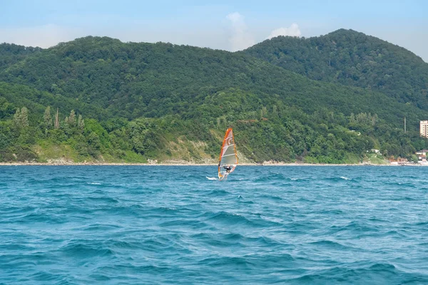 Windsurfing in the sea, water sports. View to windsurfer and green mountains.