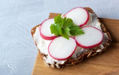 Ev yapımı çavdar ekmeği kaymak peyniri, turp, ricotta ve bitkilerle ahşap kesim tahtasında..