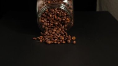 Slow motion shot of coffee beans falling from the glass jar
