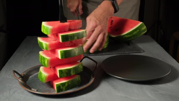 Жінка ріже кавун і кладе шматки на тарілку Жінка готує солодкий фруктовий десерт для пікніка — стокове відео