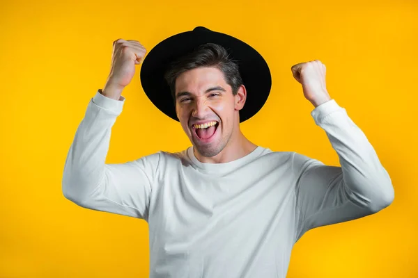 Hipster homme en chapeau est très heureux et heureux, il montre oui geste de victoire, gars a obtenu le résultat, objectifs. Surpris heureux garçon excité sur fond jaune — Photo