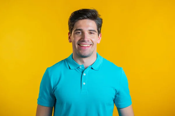 Portrait d'un beau et souriant homme en t-shirt bleu regardant vers la caméra. Guy en studio sur fond jaune vif. — Photo