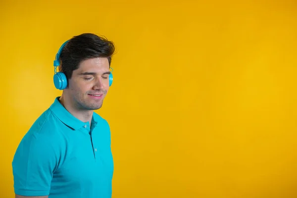 Knappe jongeman met trendy kapsel die plezier heeft, lacht, danst met een blauwe hoofdtelefoon in de studio tegen een gele achtergrond. Muziek, dans, radio concept. — Stockfoto