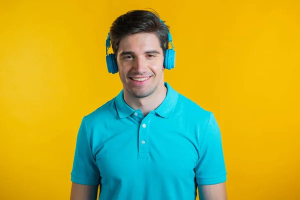 Knappe jongeman met trendy kapsel die plezier heeft, lacht, danst met een blauwe hoofdtelefoon in de studio tegen een gele achtergrond. Muziek, dans, radio concept. — Stockfoto