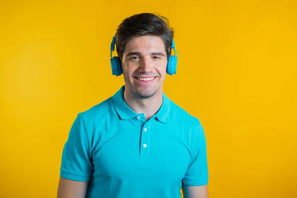 Beau jeune homme à la coiffure tendance s'amusant, souriant, dansant avec des écouteurs bleus en studio sur fond jaune. Musique, danse, concept radio. — Photo