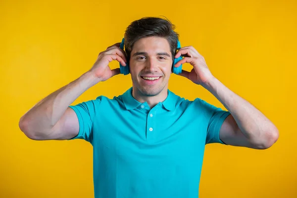 Schöner junger Mann mit modischer Frisur, der Spaß hat, lächelt und mit blauen Kopfhörern im Studio vor gelbem Hintergrund tanzt. Musik, Tanz, Radiokonzept. — Stockfoto