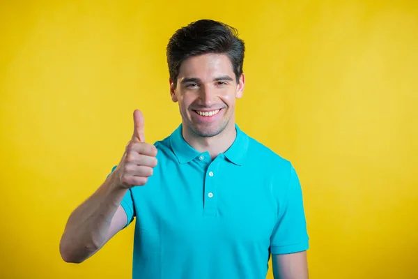 Un hombre guapo muestra los pulgares hacia arriba, como gesto. Chico feliz sobre fondo amarillo. Ganador. Éxito. Modelo masculino positivo sonríe a la cámara. Lenguaje corporal. — Foto de Stock