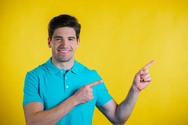 Happy smiling man presenting and showing something isolated on yellow background. Portrait of guy, he pointing with arms on her left with copy space. — Stock Photo, Image