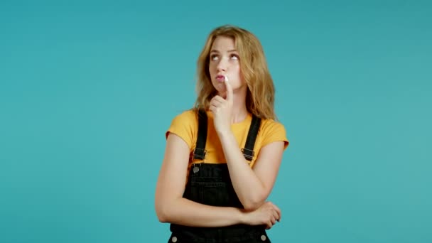 Mujer pensante mirando hacia arriba y alrededor sobre fondo azul. Expresiones faciales pensativas. Bonito modelo con apariencia atractiva — Vídeos de Stock