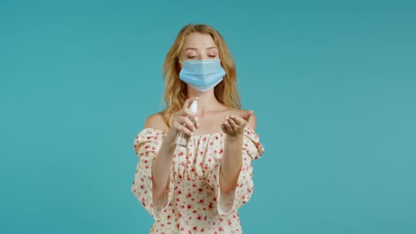 Vrouw met beschermend masker brengt ontsmettingsmiddel antiseptisch aan op haar handen. Stop virus concept, bacteriële bescherming. Blauwe studio achtergrond. — Stockvideo