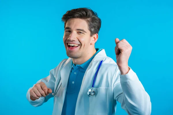 Uśmiechnięty doktor zabawny taniec, sukces i szczęście w pracy. młody przystojny Doc człowiek w profesjonalny medyczny biały płaszcz jest odizolowany na niebieskim tle studio. — Zdjęcie stockowe