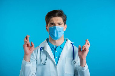 Maskeli yakışıklı doktor mavi arka plan için dua ediyor. Adam birine arzularını tatmin etmesi için yalvarıyor..