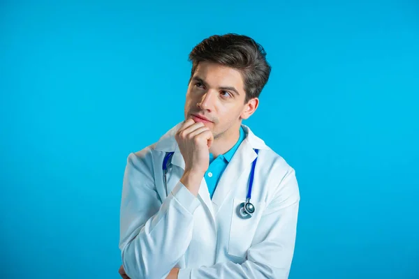 Denkender Arzt, der auf blauem Hintergrund auf- und umblickt. Besorgte nachdenkliche Mienen. Schöner Doktor im Arztkittel mit Stethoskop — Stockfoto