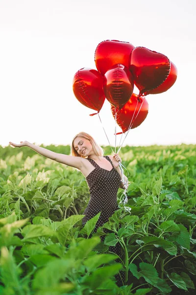 Красива жінка в ретро-червоній сукні позує з повітряними кулями у формі серця в зеленому полі. День народження, свято, святкування концепції свободи . — стокове фото