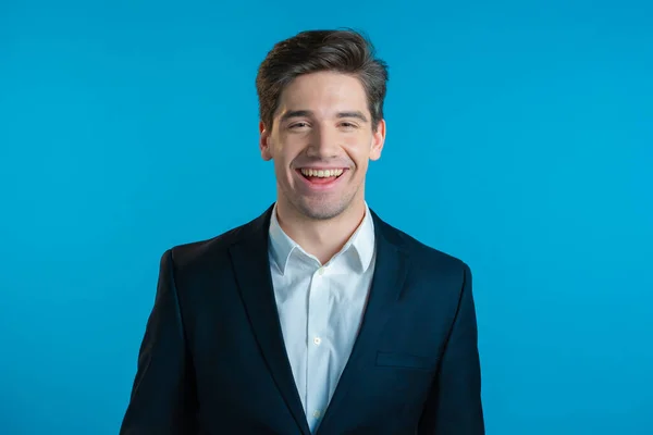 Portrét mladého úspěšného sebevědomého podnikatele izolovaného na modrém pozadí studia. Muž v obleku, dívá se do kamery a usmívá se. Portrét pohledného chlapa. — Stock fotografie