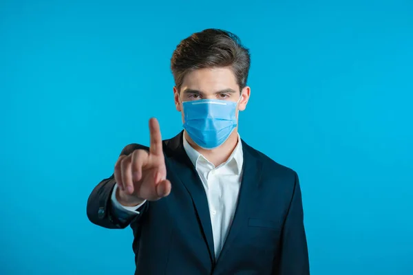 Retrato de empresario serio en traje profesional y máscara médica que muestra gesto de rechazo por señal de stop finger. Hombre aislado sobre fondo azul. — Foto de Stock