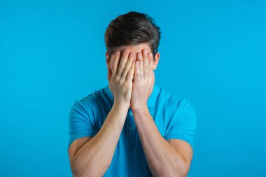 Genç bir adamın facepalm hareketi yaparken portresi, hayır, unuttum. Mutsuz adam üzüntü, pişmanlık, drama, başarısızlık hissediyor. Mavi duvarda izole edilmiş.